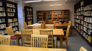 Interior of a library with wooden tables and chairs in the middle of several bookshelves full of books