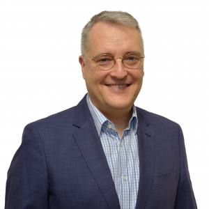 A smiling man wearing glasses, a navy blue blazer, and a collared shirt
